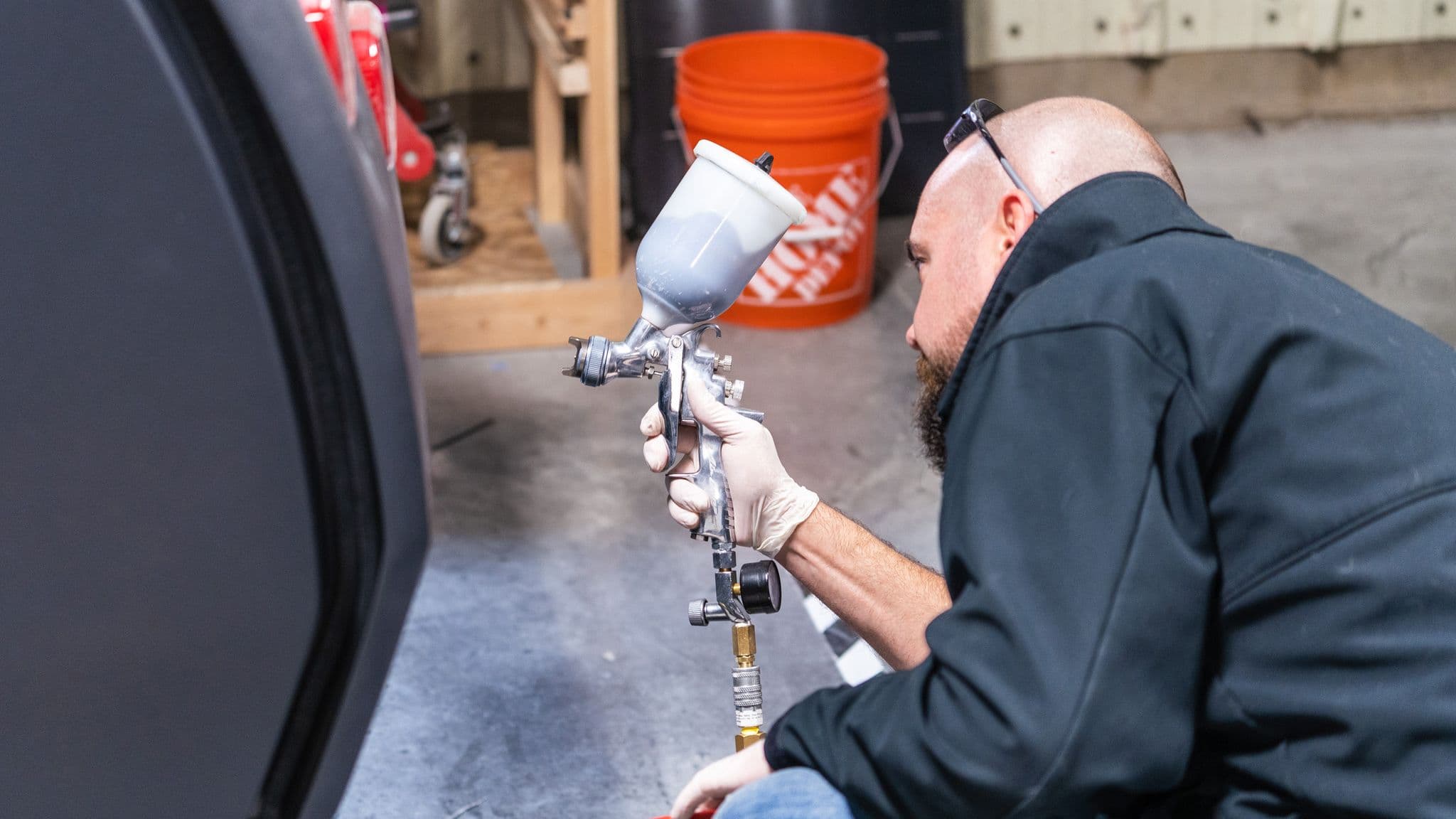 A technician in a black jacket and gloves carefully applies a spray coating to an Escapod trailer using a professional spray gun inside the factory.
