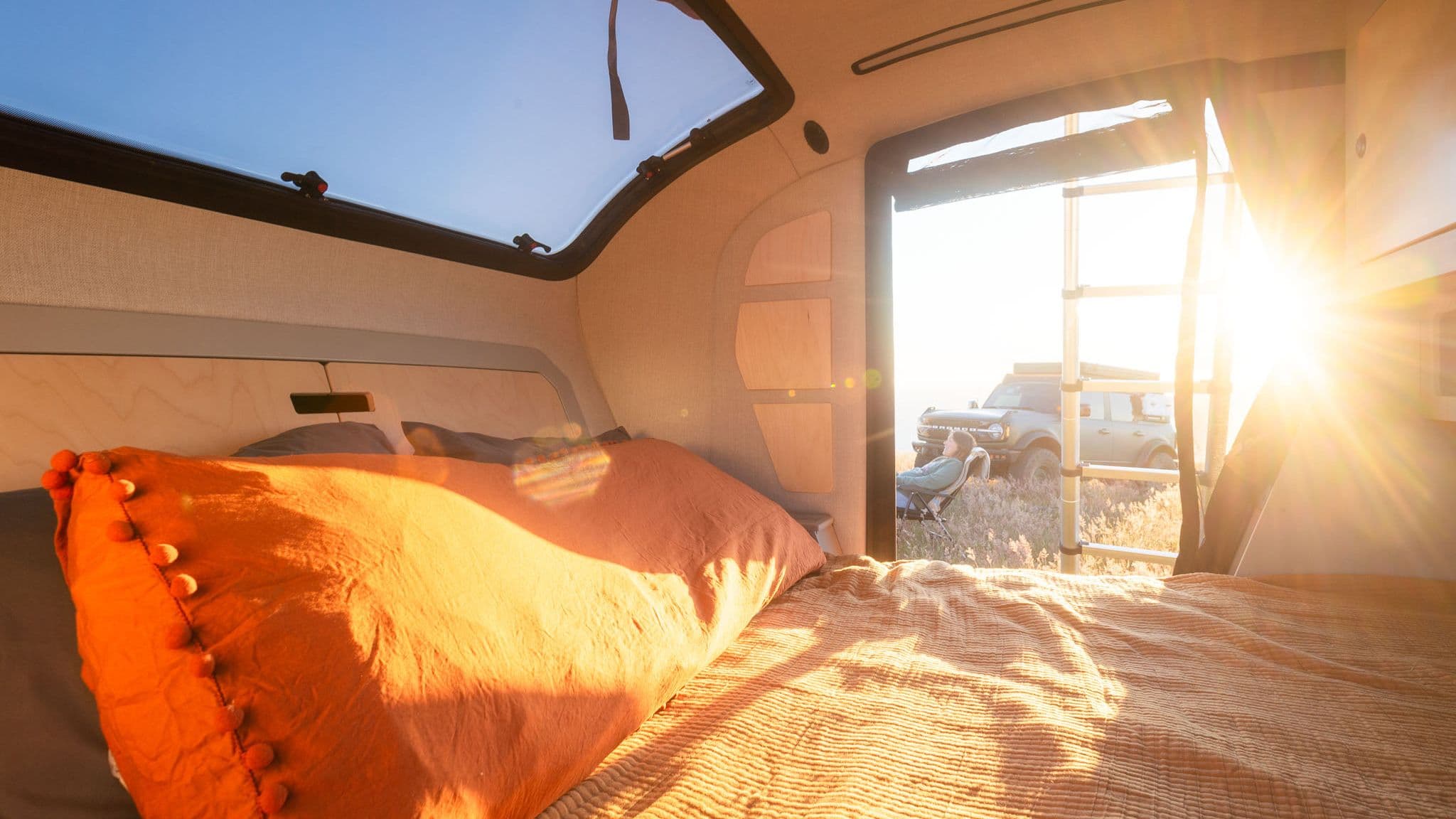 Cozy interior of an Escapod TOPO2 trailer with sunlight streaming in, showing the bed and an open door.