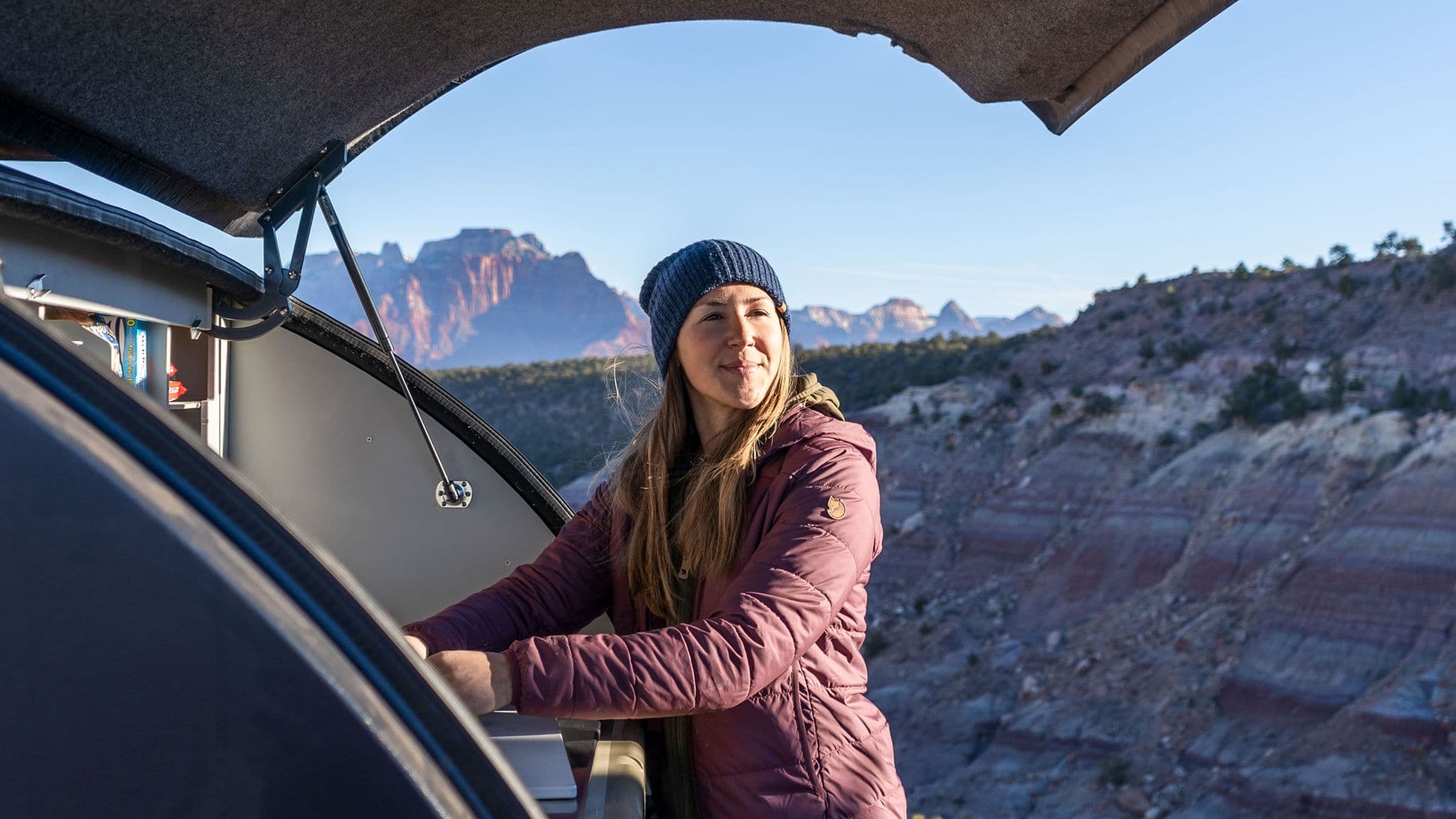 Camper enjoys breakfast in the open-air galley of an Escapod trailer, taking in the expansive red rock desert views under a clear blue sky.